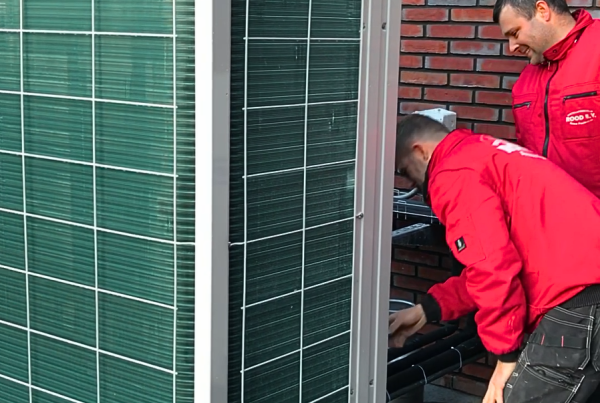 Twee monteurs van Rood installeren een buitenunit van een airconditioningsysteem op een plat dak.
