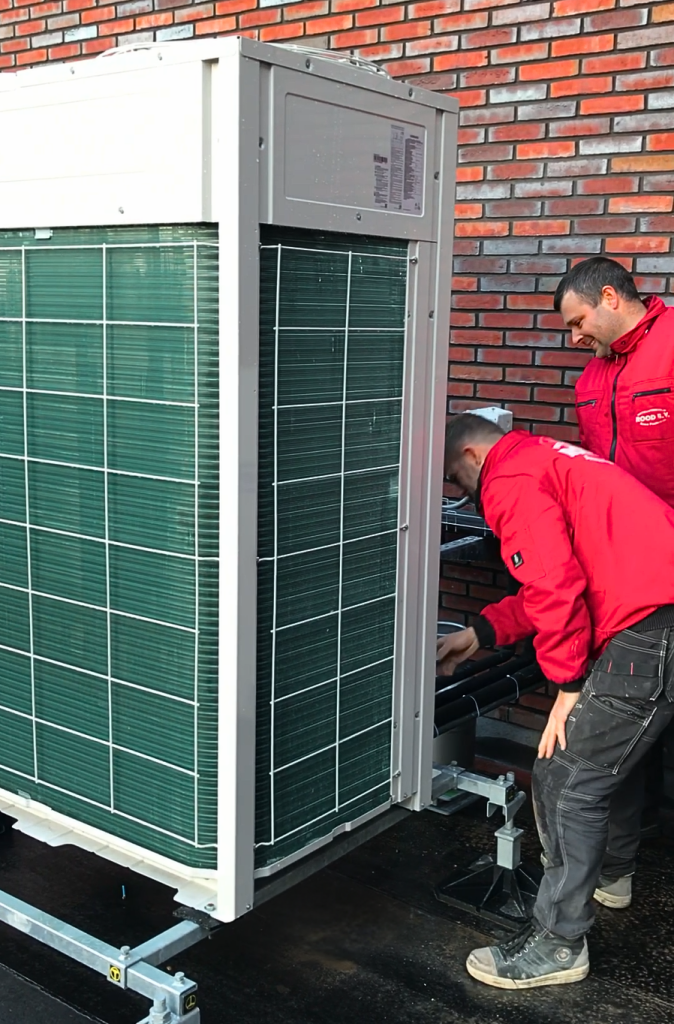 Twee monteurs van Rood installeren een buitenunit van een airconditioningsysteem op een plat dak.